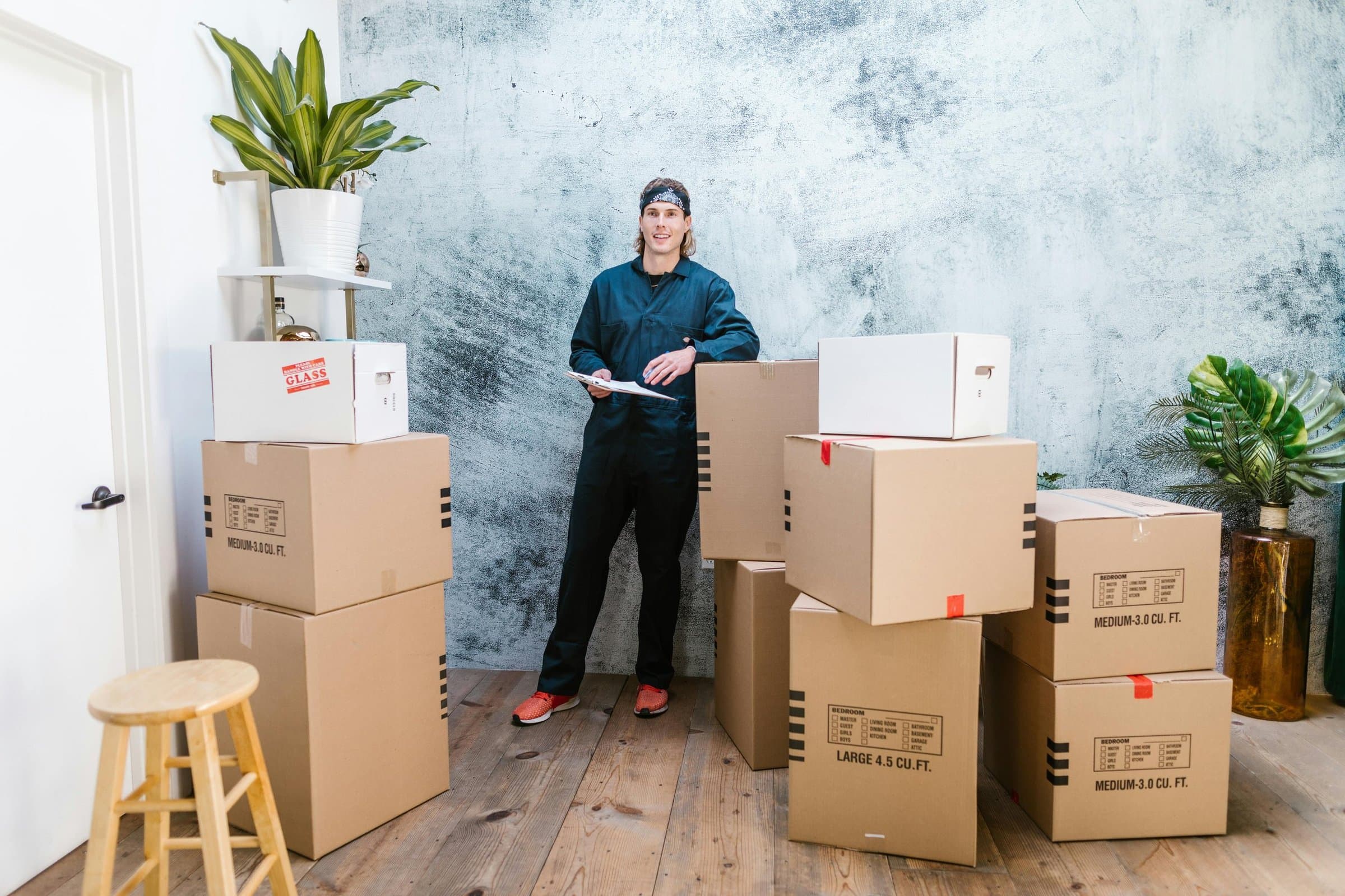 A mover in overalls holding a clipboard among stacked moving boxes