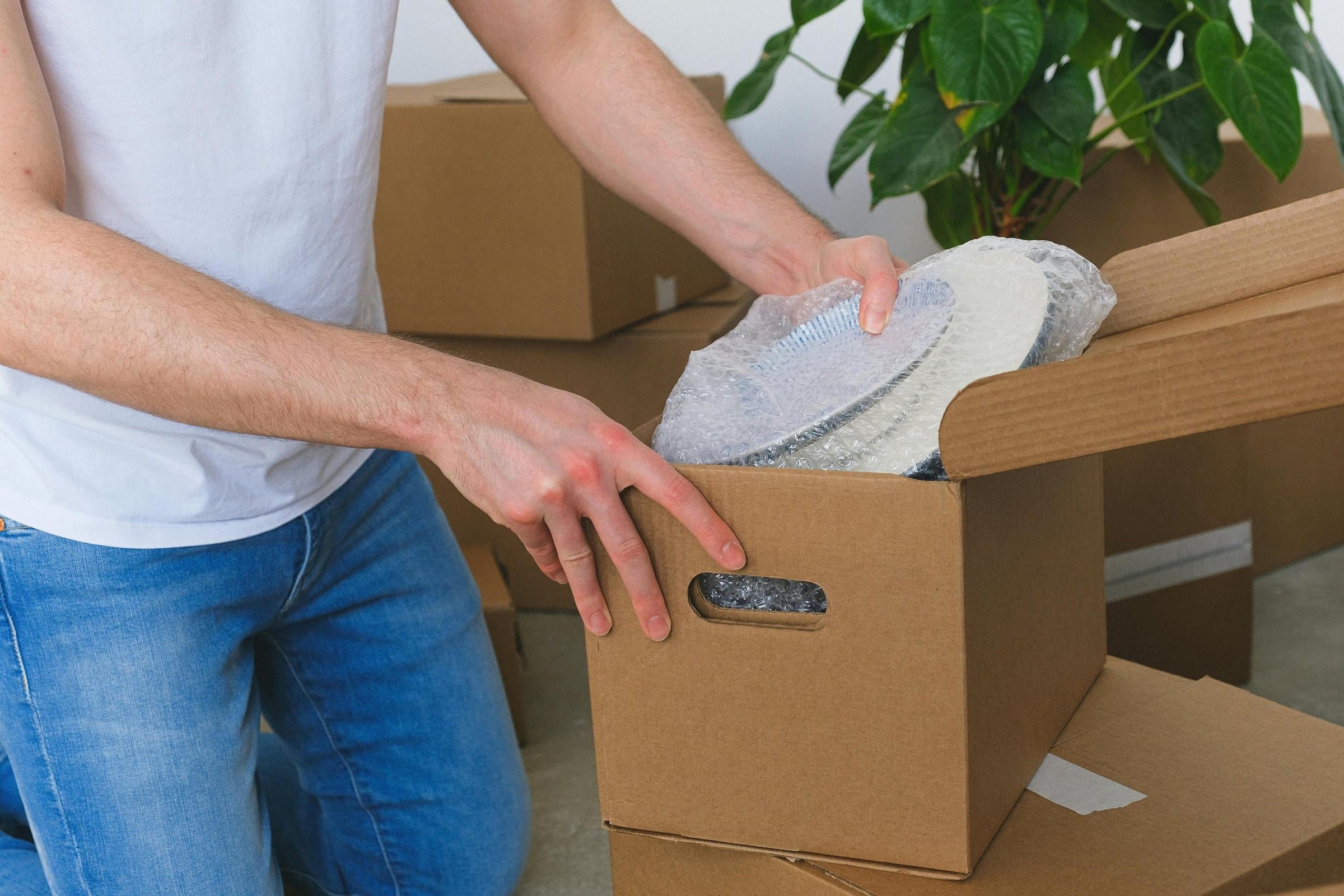 A man packing bubble-wrapped plates into a moving box