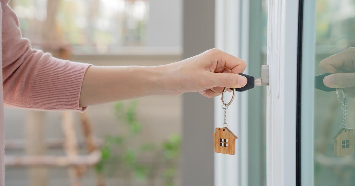 A hand turning a key with a house-shaped keyring in a door