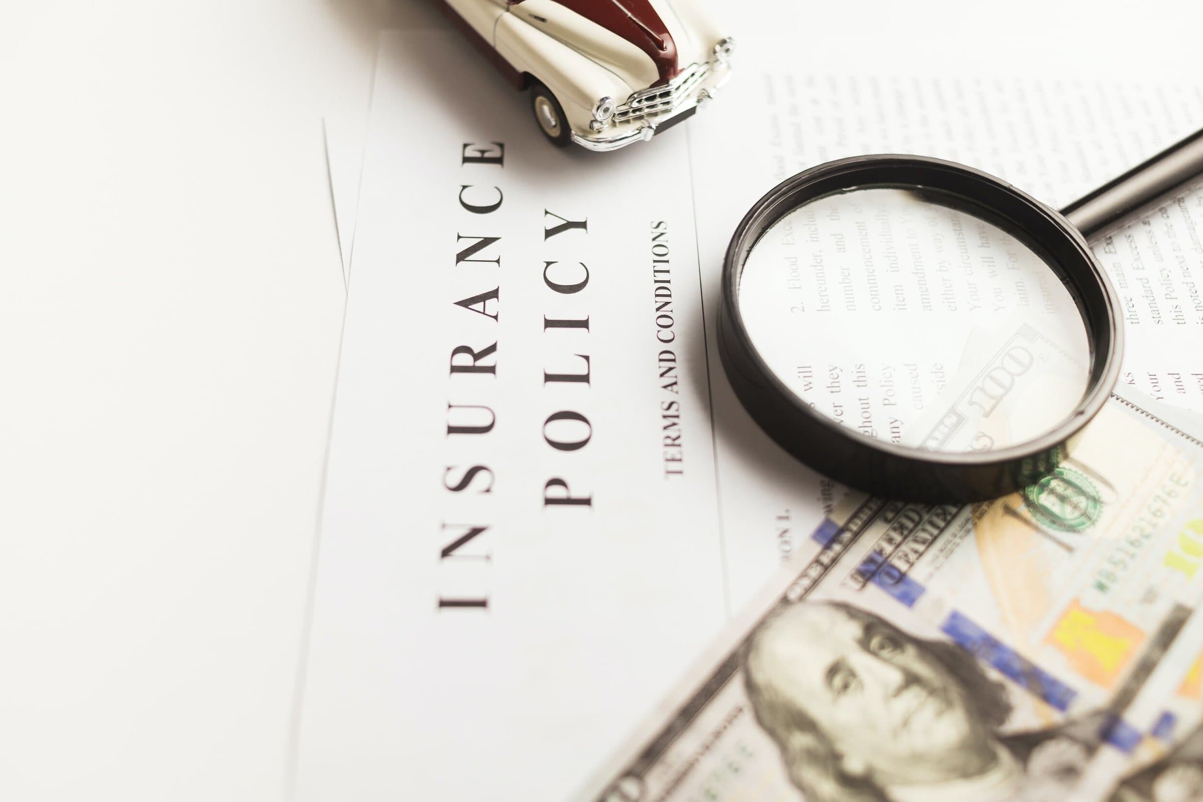 An insurance policy document with a magnifying glass, banknotes and a toy car