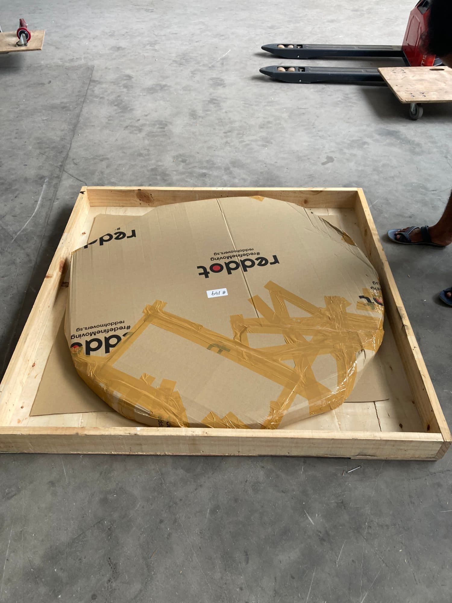 A round tabletop wrapped in Reddot cardboard, set in a wooden crate for shipping