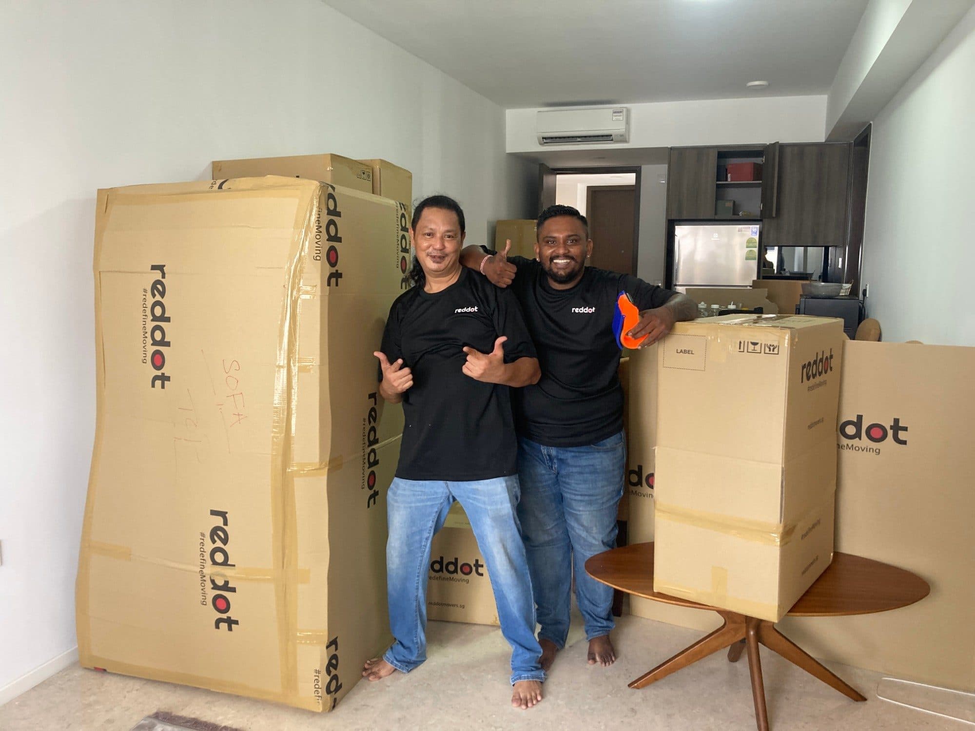 Two smiling Reddot movers giving a thumbs up among packed Reddot boxes