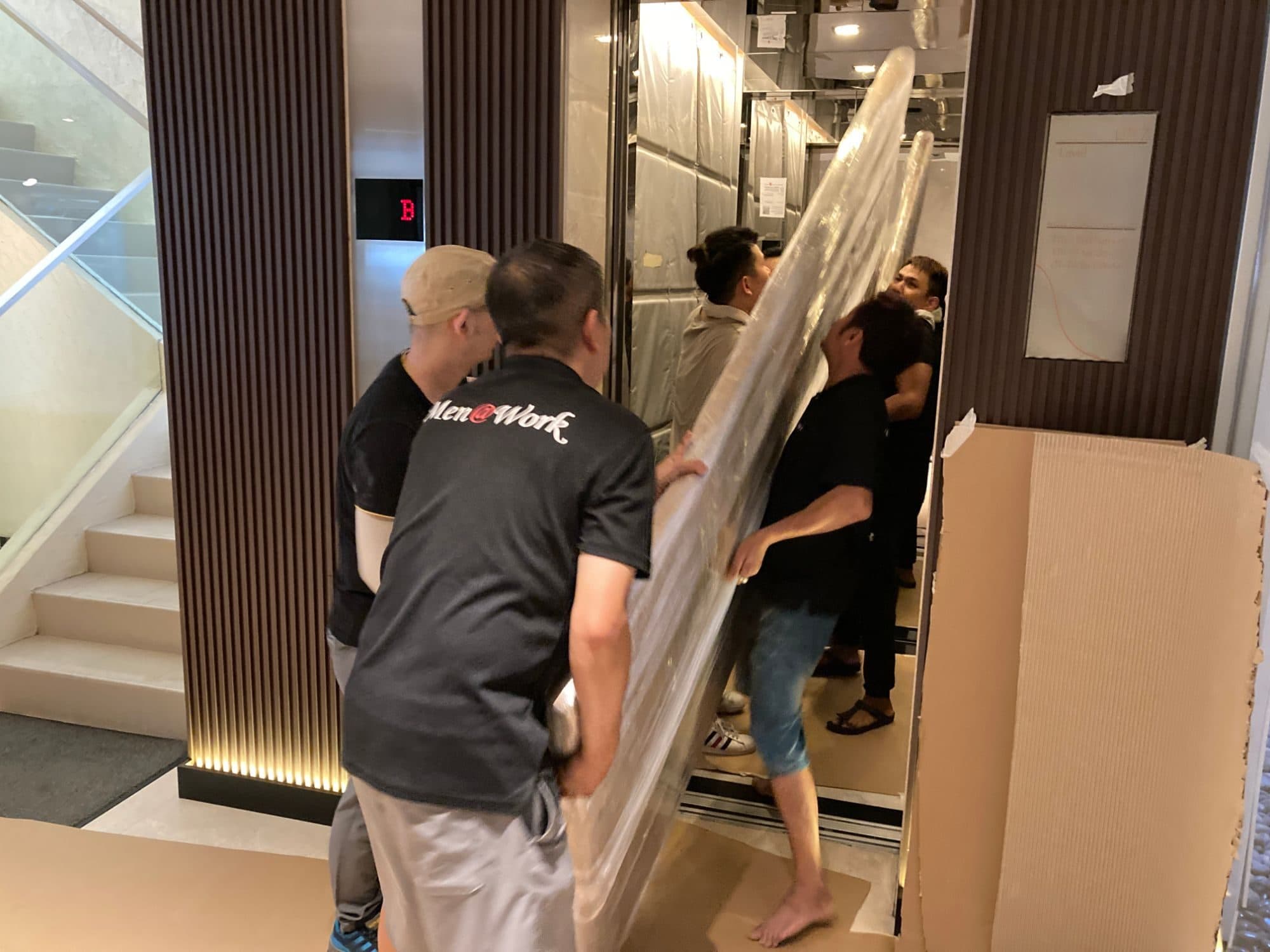 Reddot movers guiding a large plastic-wrapped item into a lift