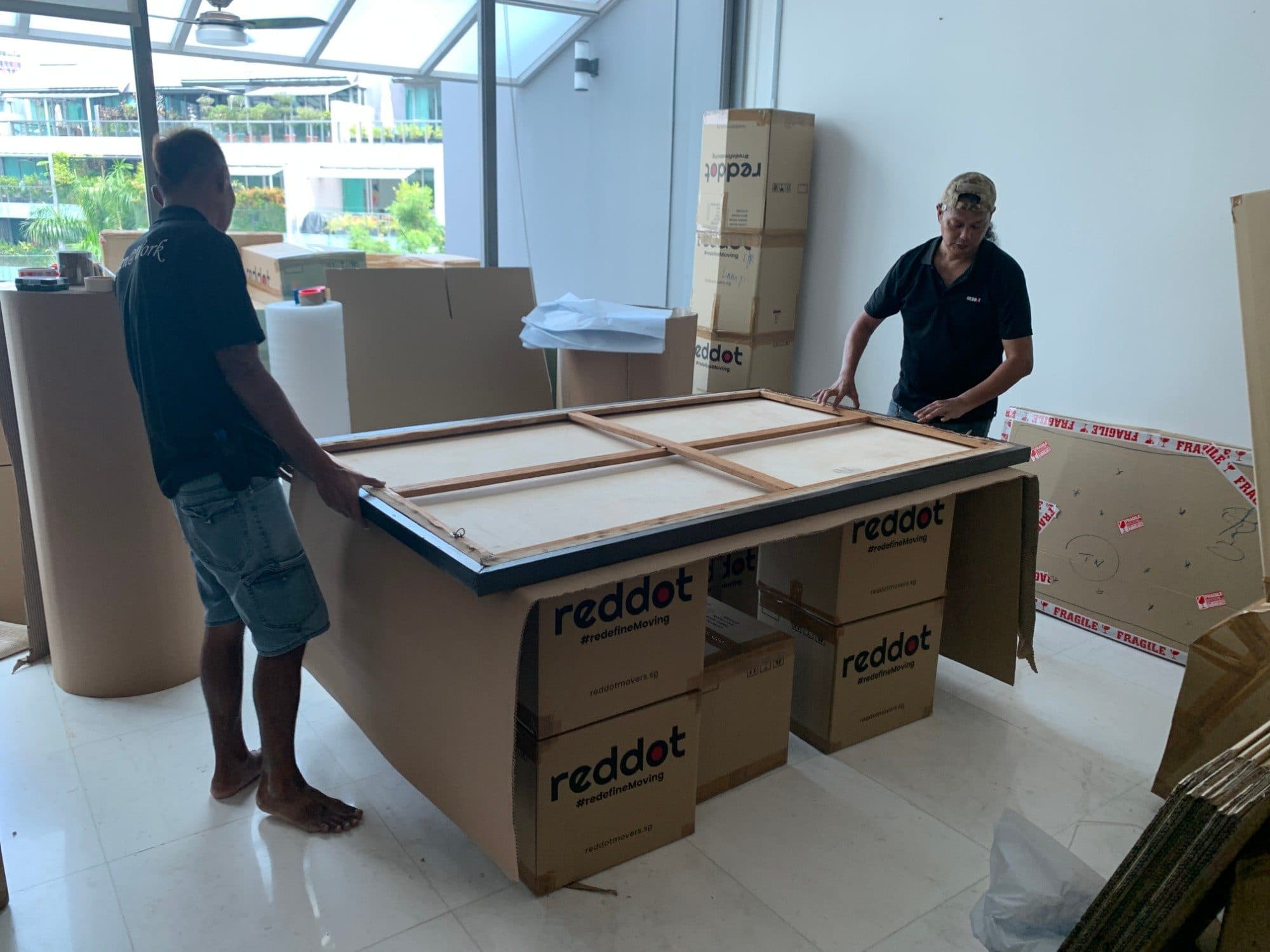 Two Reddot packers placing a large framed artwork face down on a padded stand of Reddot boxes