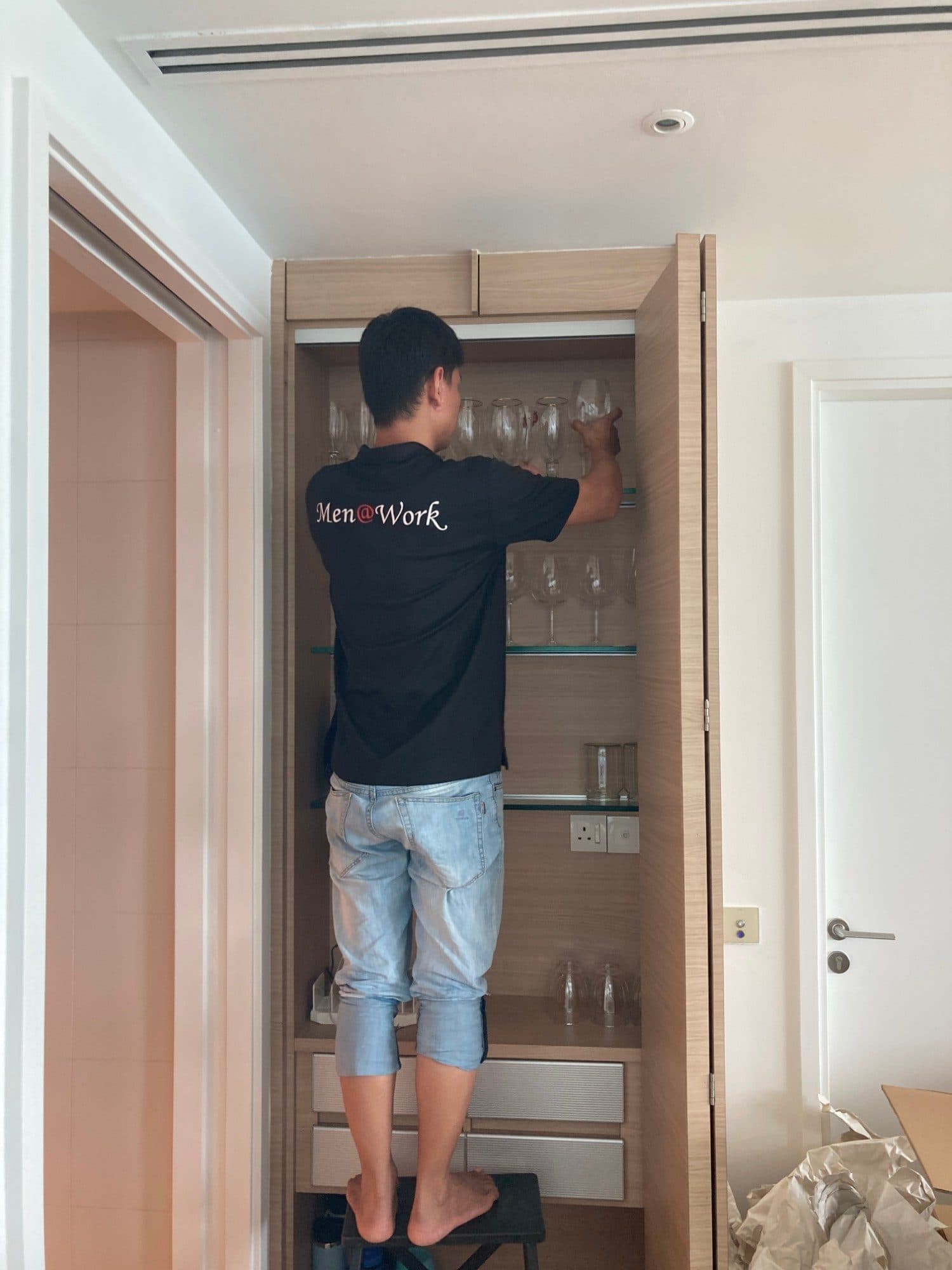 A Reddot packer on a step stool taking wine glasses from a cabinet