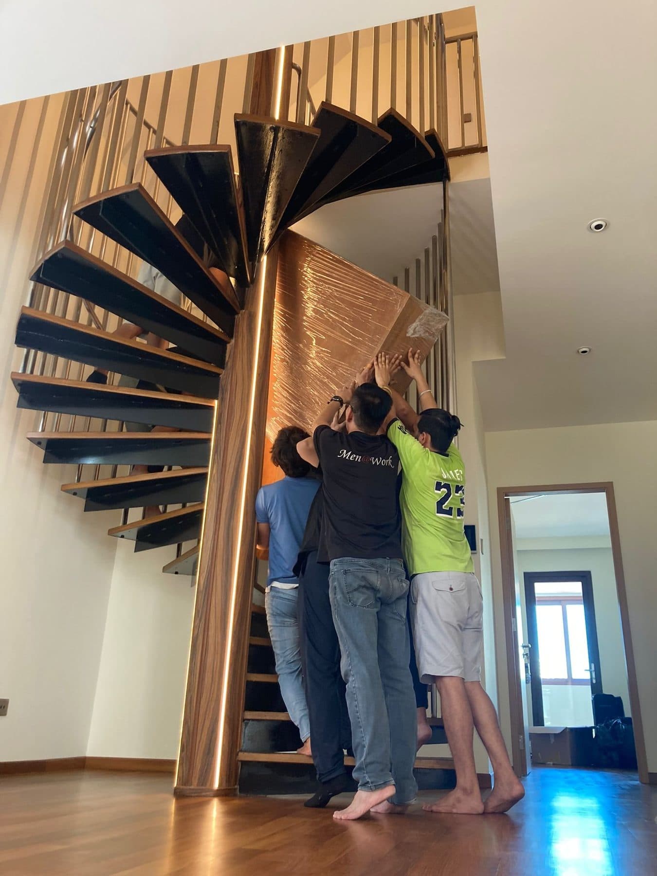 Movers lifting a wrapped item up a spiral staircase