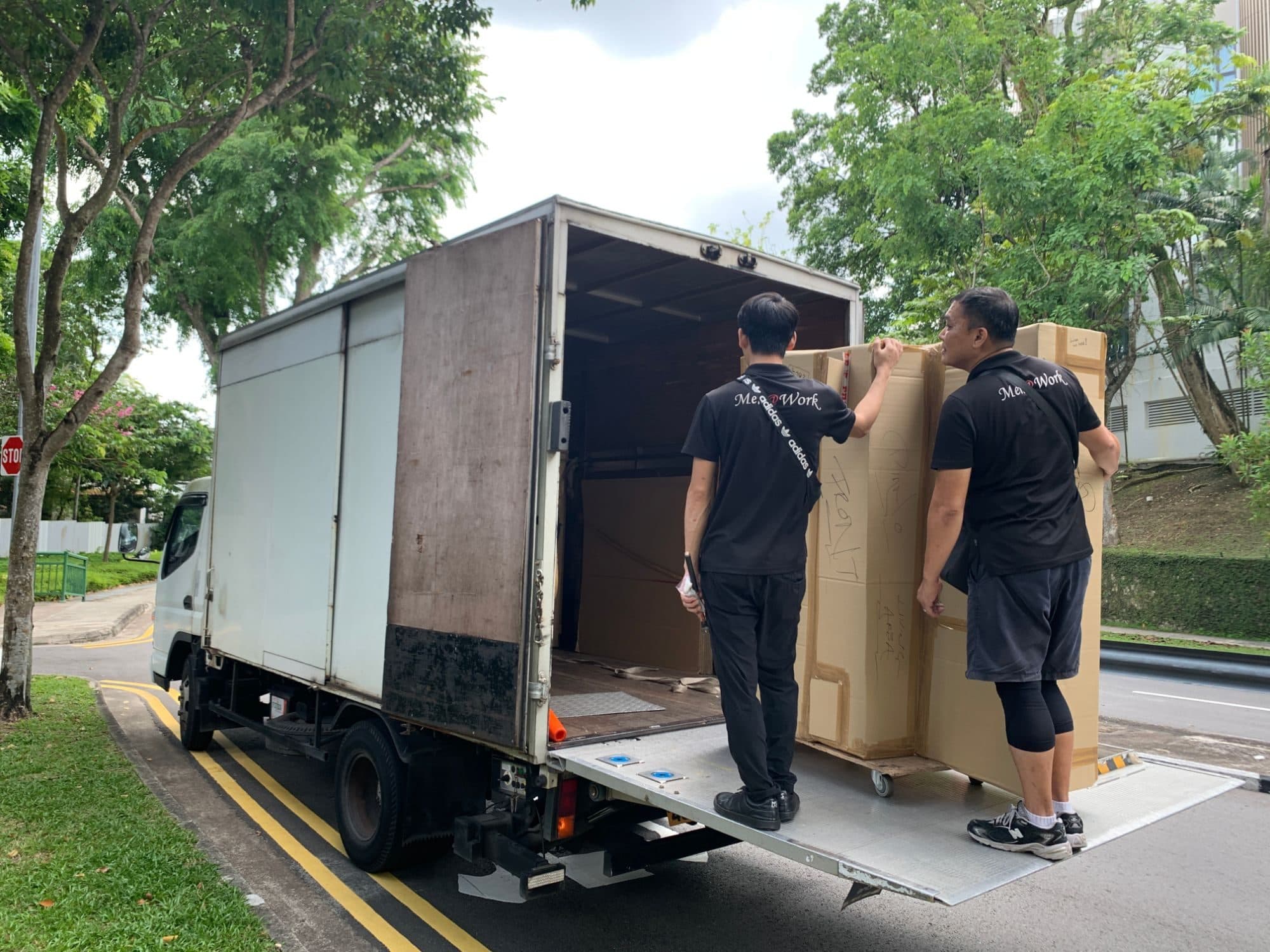 Two Reddot movers rolling a tall boxed item onto the tail-lift of a moving truck