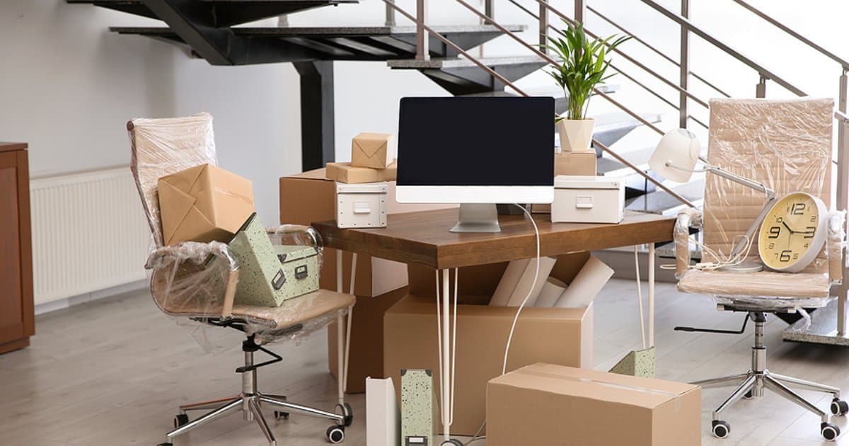 An office mid-move, with chairs wrapped in plastic and boxes around a desk