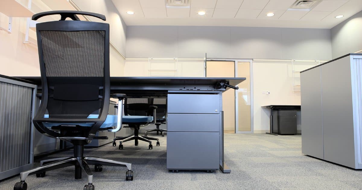 An empty office with desks, cabinets and a mesh office chair