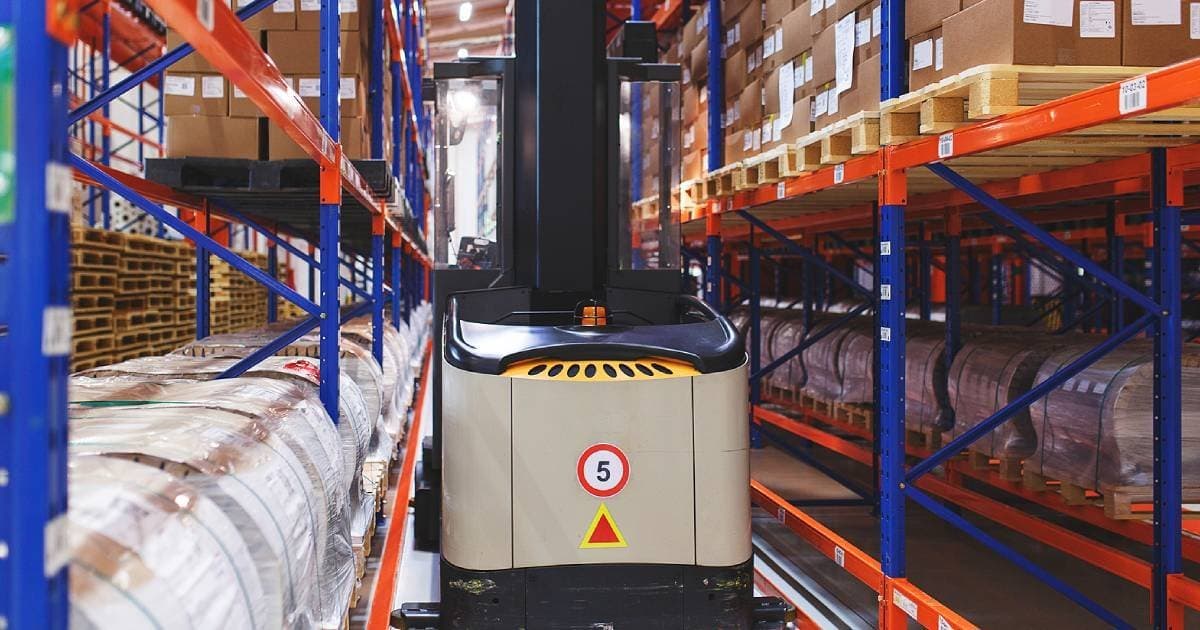 A forklift in a warehouse aisle between tall racks of stored goods