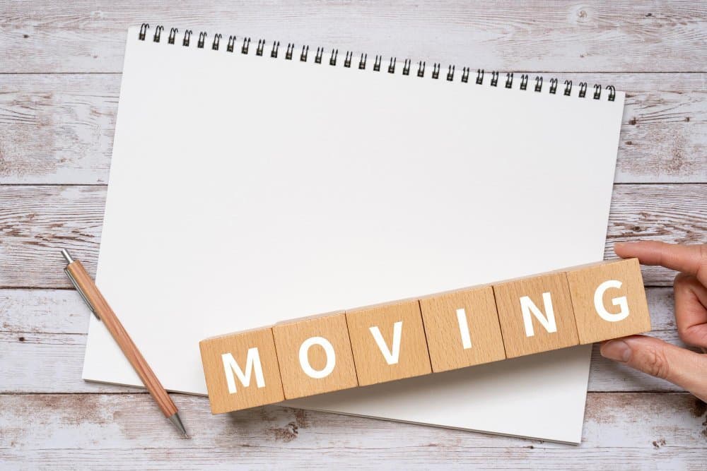 Wooden blocks spelling “moving” on a notepad beside a pen