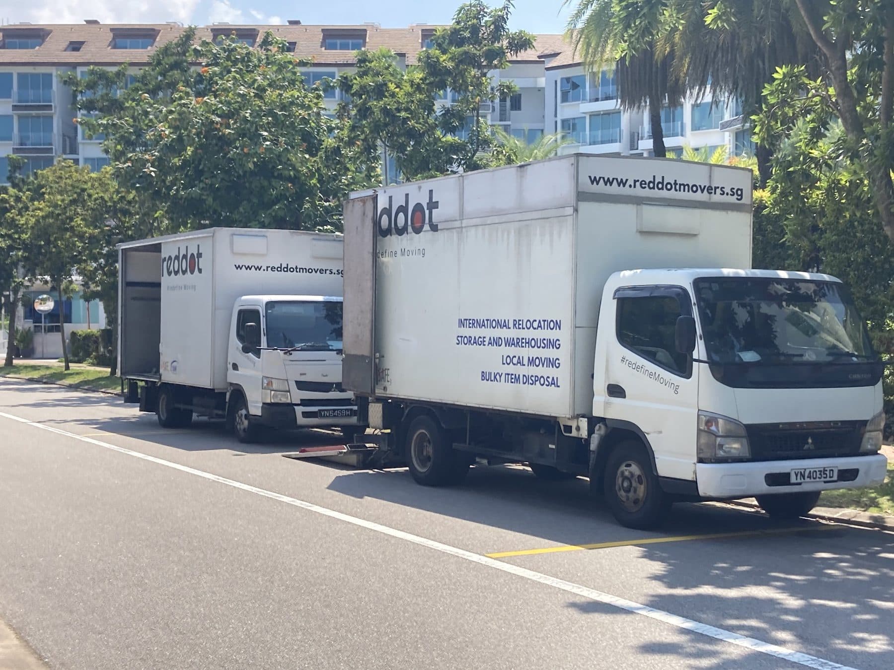 Two Reddot trucks parked on a sunny road beside condominiums